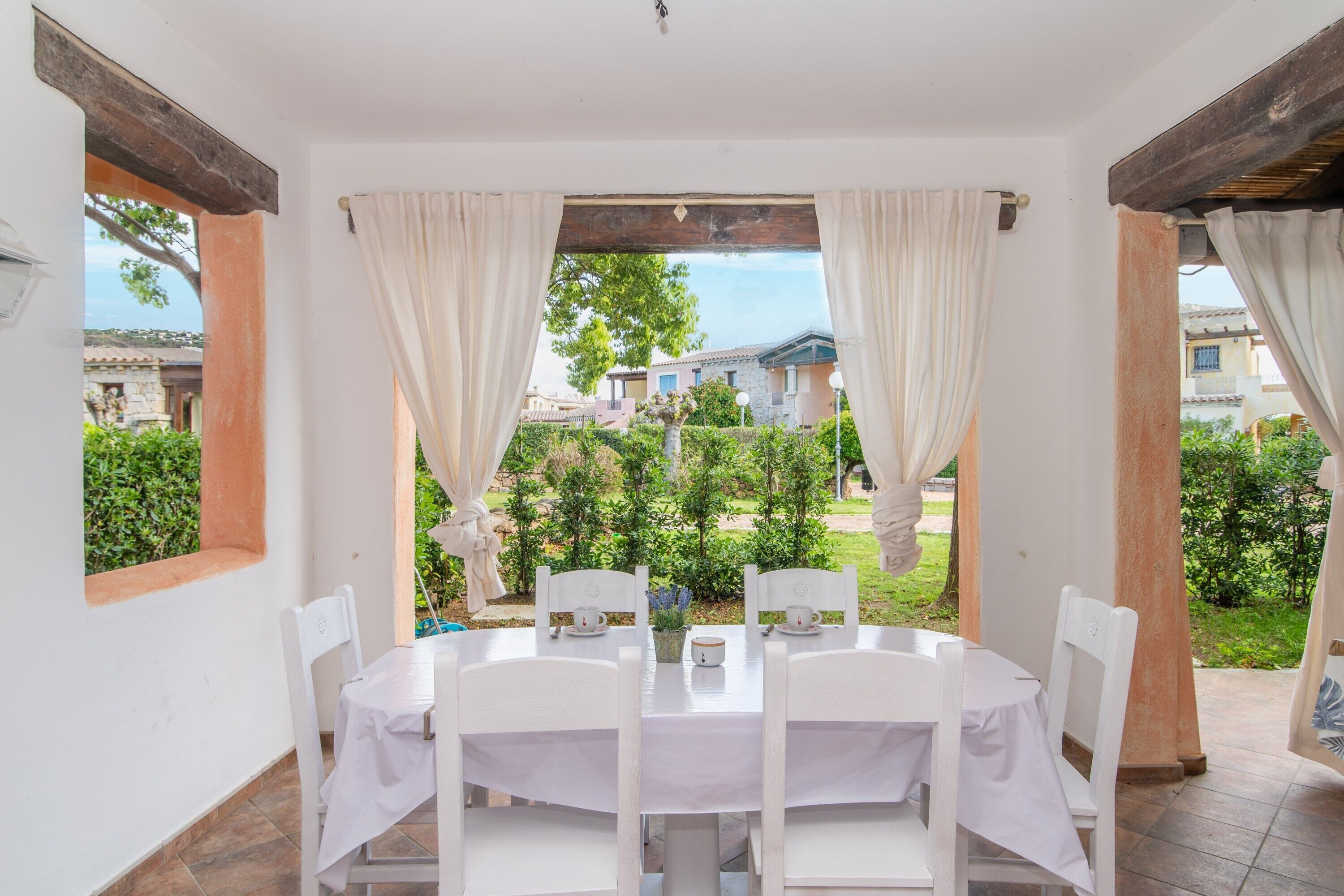 Un espace repas comprenant une table et des chaises, avec vue sur la verdure et les bâtiments environnants, et agrémenté d’une pergola.