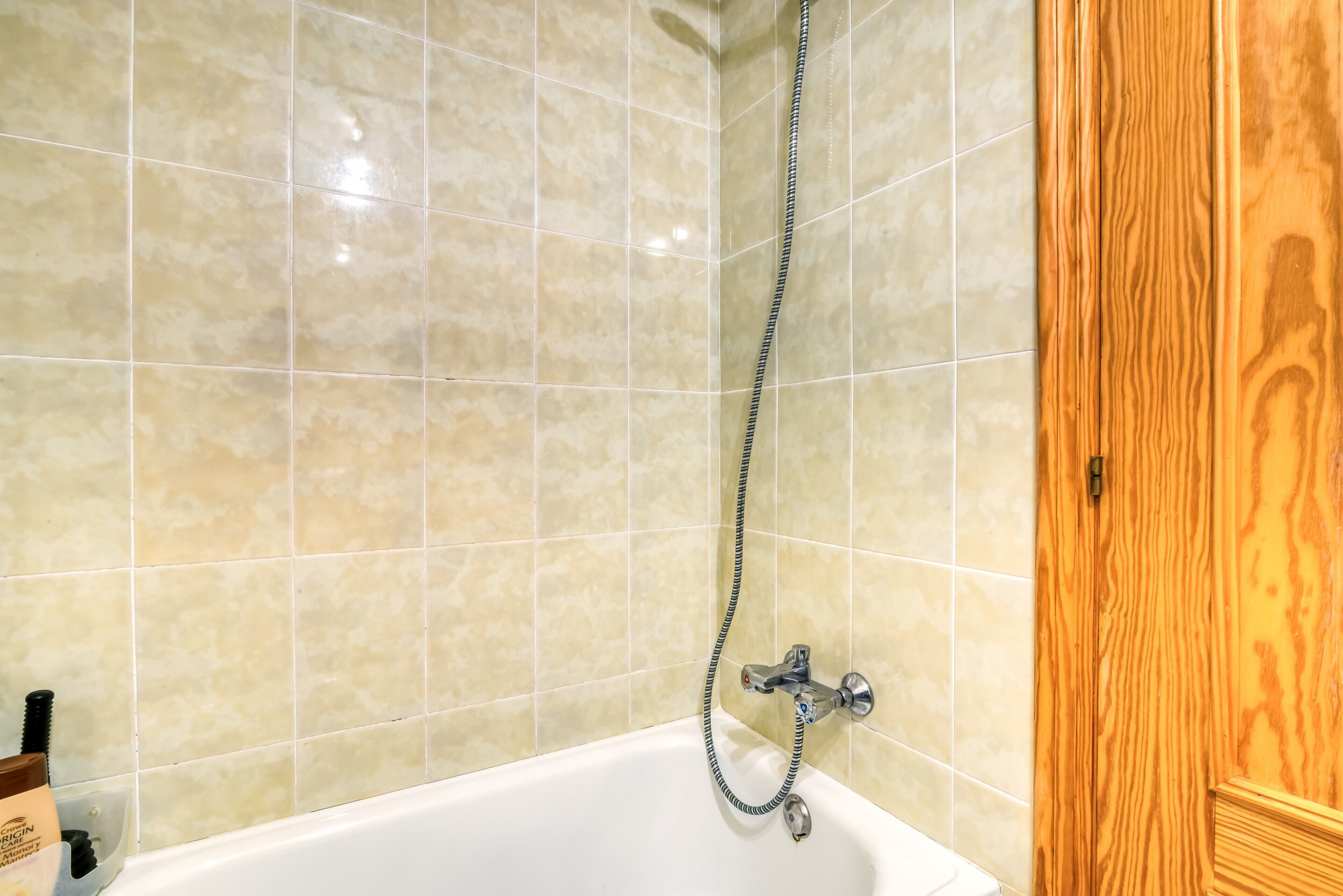 A bathroom with beige tiled walls, a white bathtub, and a wooden door.