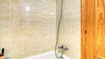 A bathroom with beige tiled walls, a white bathtub, and a wooden door.