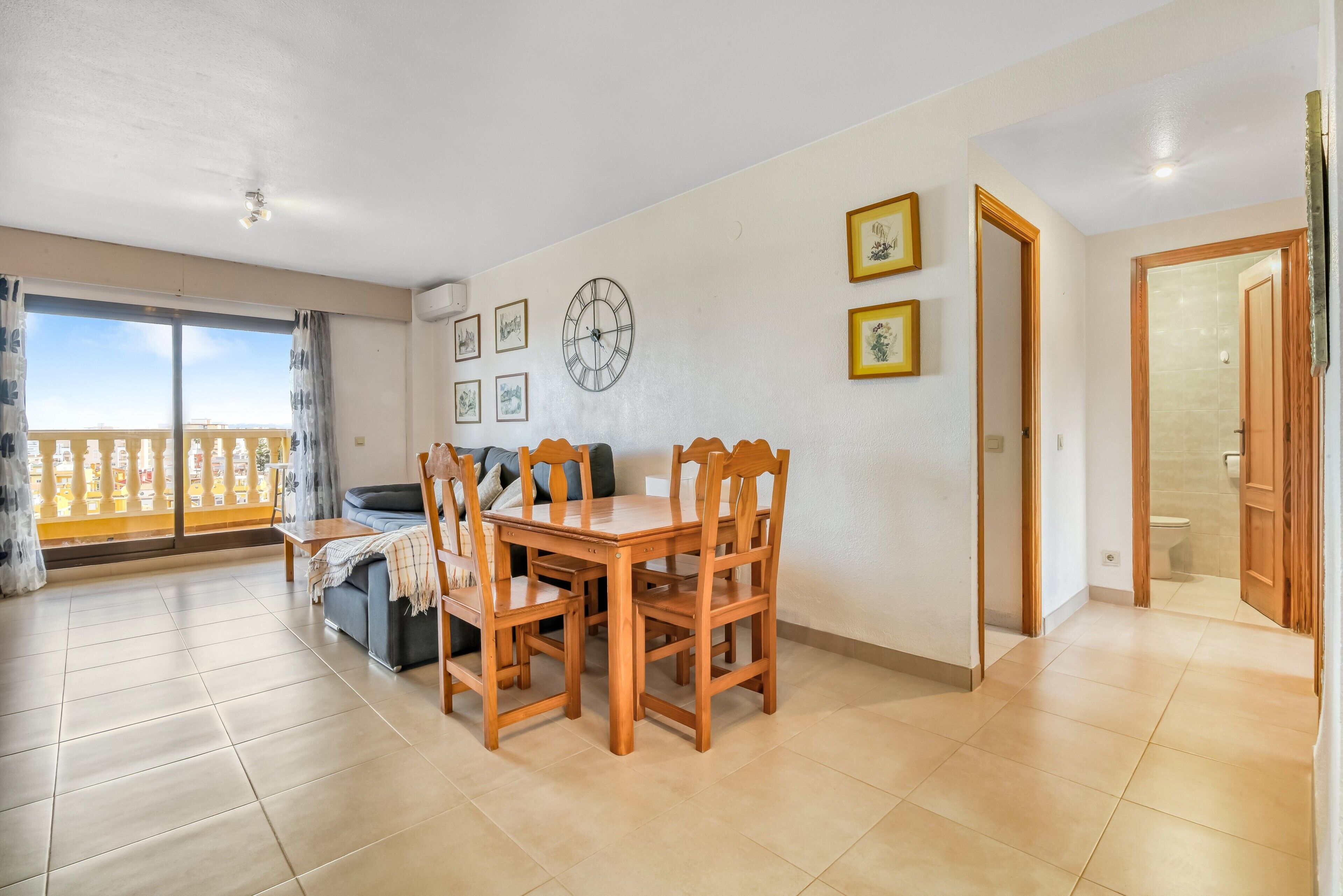 A dining area with a wooden table and chairs, a sofa, and a balcony with a railing.
