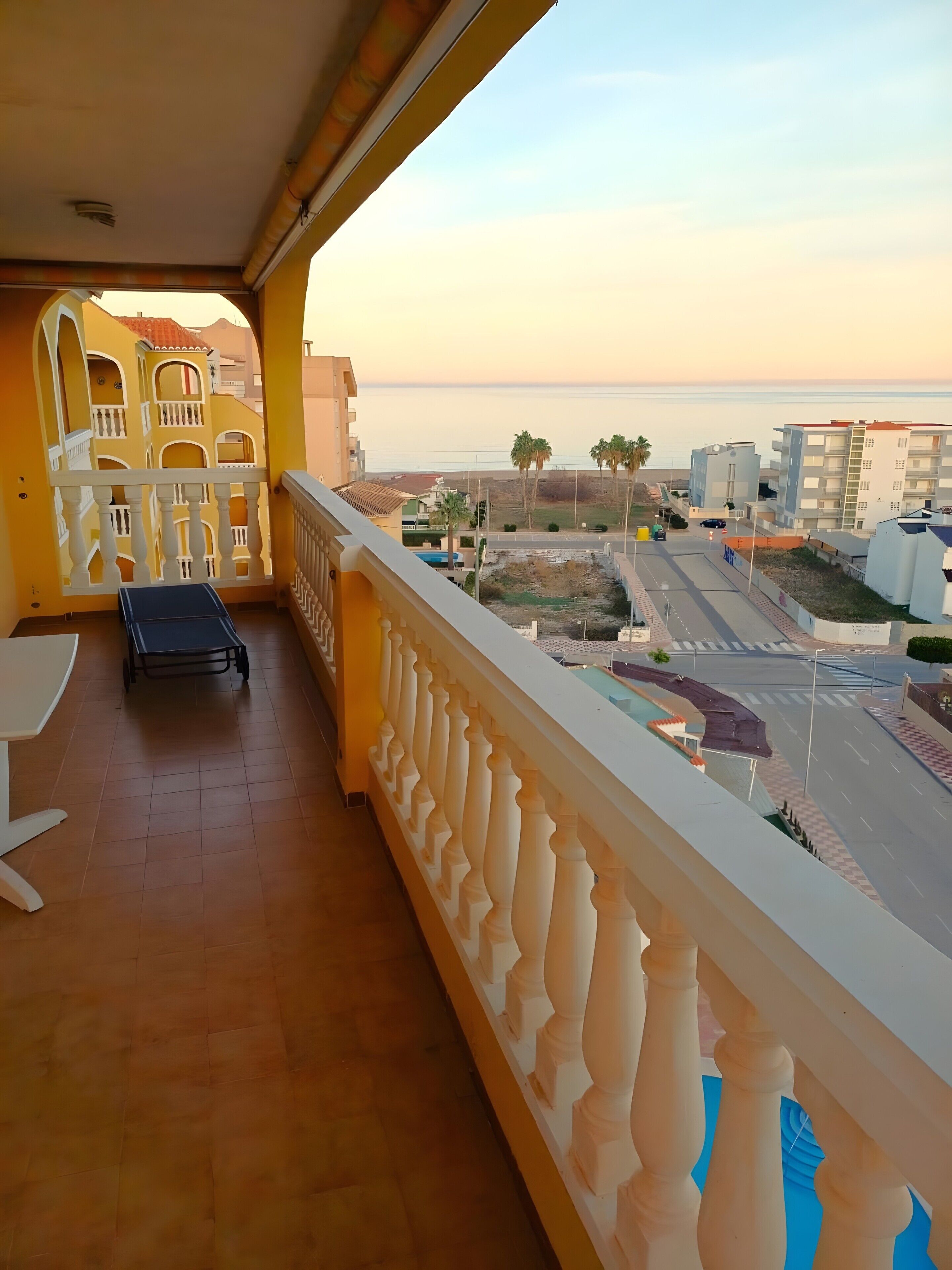 Un balcon avec vue sur la mer, une balustrade blanche et un fauteuil de relaxation.