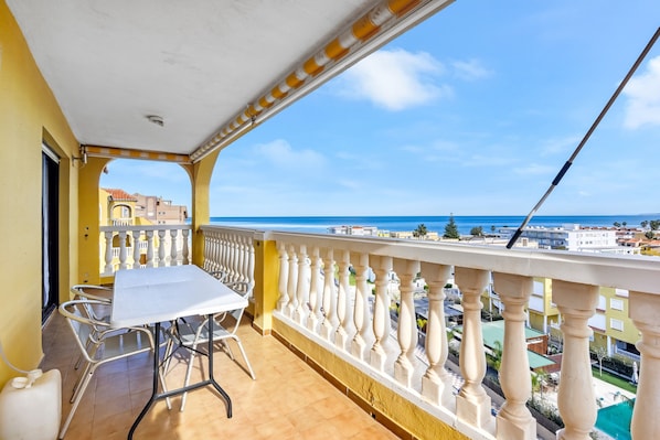 Un balcone con tavolo e sedie, una ringhiera e vista sul mare e sugli edifici.
