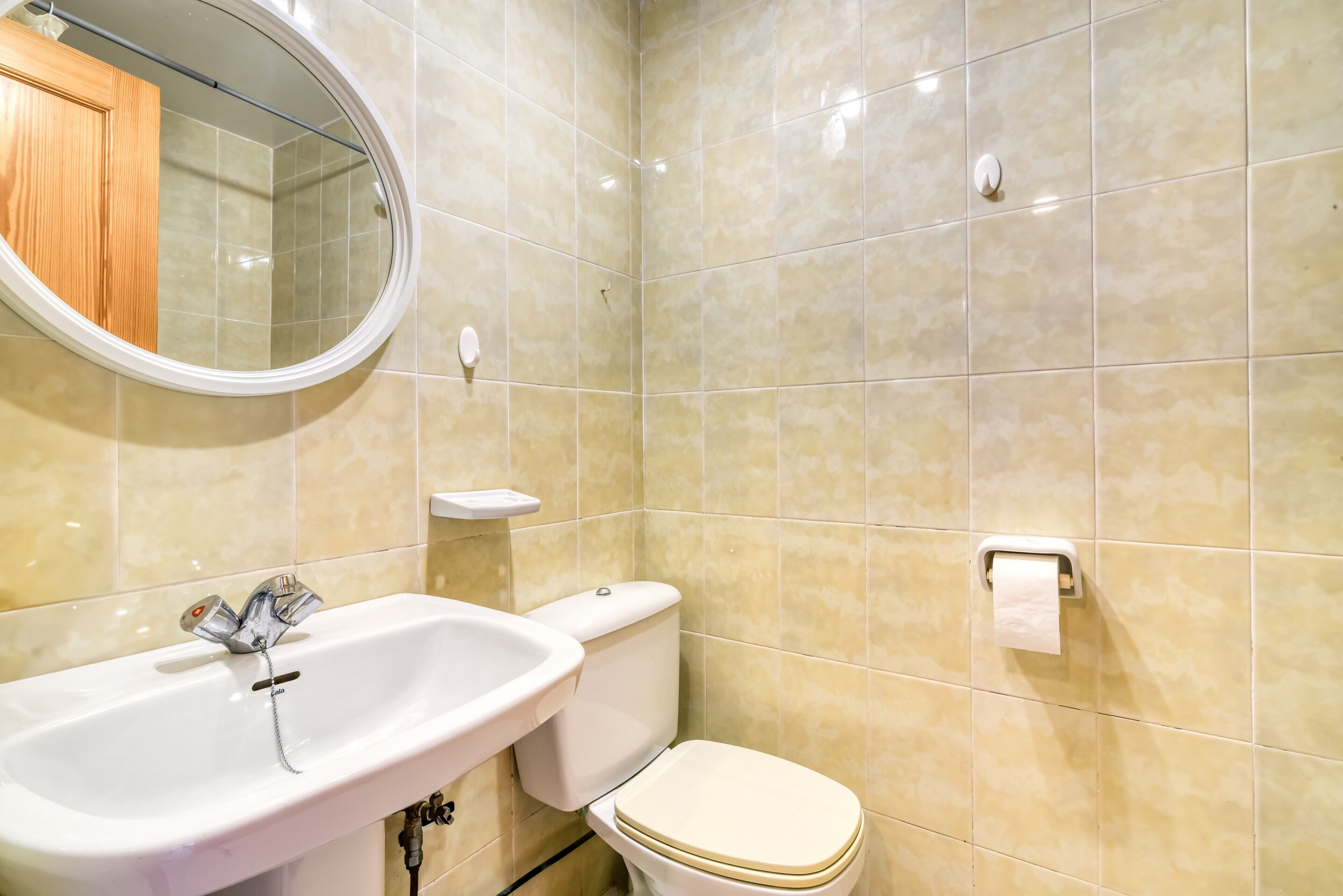 Un baño con lavabo, inodoro, espejo y paredes con azulejos.