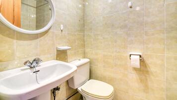Un baño con lavabo, inodoro, espejo y paredes con azulejos.