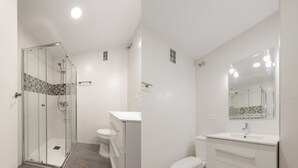 Ein modernes Badezimmer mit Duschkabine aus Glas, einer weißen Toilette und einem Waschtisch mit Spiegel.