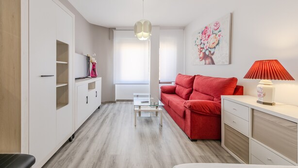 Ein modernes Wohnzimmer mit einem roten Sofa, einem Glastisch, einem weißen Schrank und einer roten Lampe.
