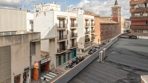 Un edificio de varios pisos con balcones, un área de estacionamiento y una iglesia con un campanario.