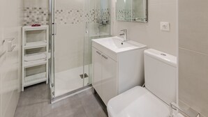 Un baño moderno con cabina de ducha de vidrio, un lavabo blanco y un inodoro.