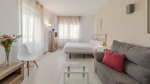 Habitación de hotel con cama, sofá, una mesita, una silla y una mesita de noche con lámpara.
