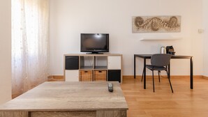 A room with a TV on a wooden stand, a dining table with a chair, and a wall-mounted artwork. - Apartment 'Chick' with Wi-Fi and Air Conditioning (Sevilla)