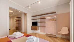 Et moderne soveværelse med seng, walk-in closet, fjernsyn og stol.