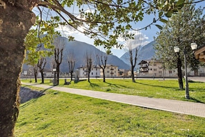 A paved walkway, trees, and buildings in a park-like setting with mountains in the background.
