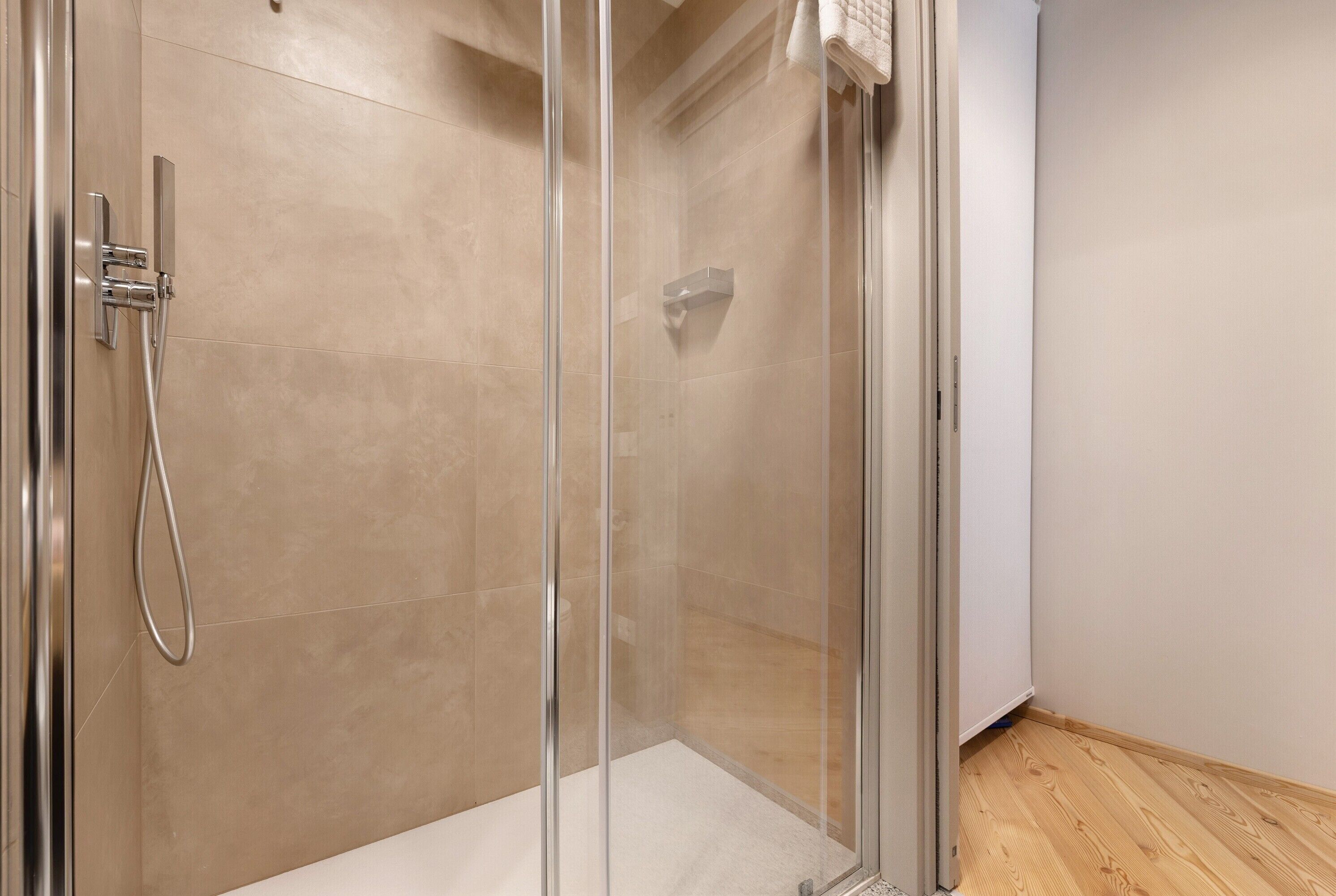 Ducha con cerramiento de vidrio, cabezal de ducha de mano y panel de control en la pared.