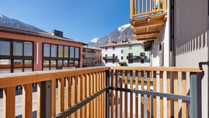 En balkon med trægelænder der kigger ud over en gade med bygninger og et bjerg i baggrunden.
