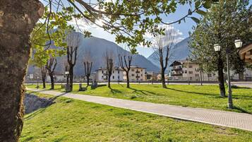 Un sendero pavimentado, árboles y edificios en un entorno similar a un parque, con montañas al fondo.