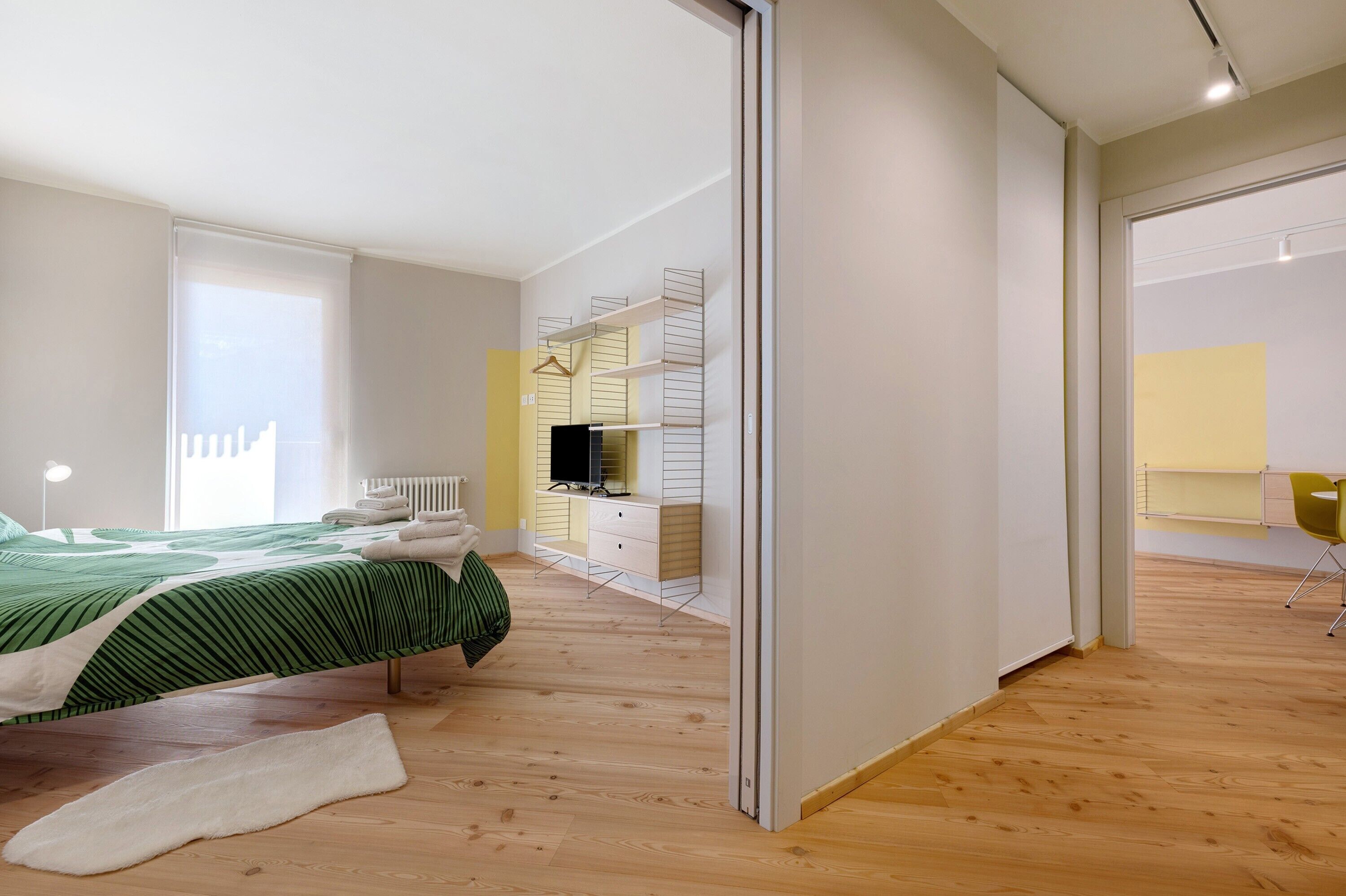 Een moderne slaapkamer met een bed, inloopkast, bureau en stoel.