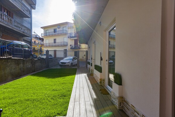 A courtyard with a wooden deck, a grassy area, and a building with a white facade and a balcony.
