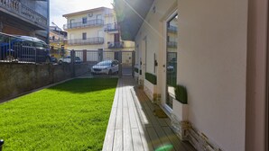 Ein Innenhof mit Holzterrasse, Rasenfläche und einem Gebäude mit weißer Fassade und Balkon.
