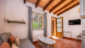 Una habitación acogedora con sofá, una mesita, una ventana con cortinas, una puerta de madera y un televisor en la pared.
