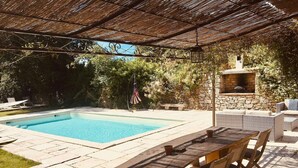 Un área de piscina con un patio de piedra, una mesa de madera con sillas y una chimenea de piedra.