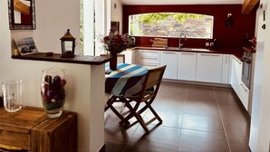 Una cocina con armarios blancos, techo de vigas de madera y un amplio ventanal con vistas a zonas verdes.