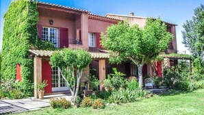 A two-story house with a red facade, a covered porch, and a well-maintained garden. - Courthézon near Avignon, holiday villa, swimming pool, beautiful park. (COURTHEZON)