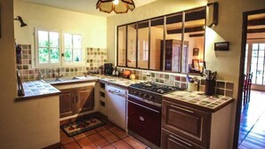 A kitchen with a gas stove, oven, and dishwasher. It has a tiled backsplash and a window with a view of greenery outside. - Courthézon near Avignon, holiday villa, swimming pool, beautiful park. (COURTHEZON)