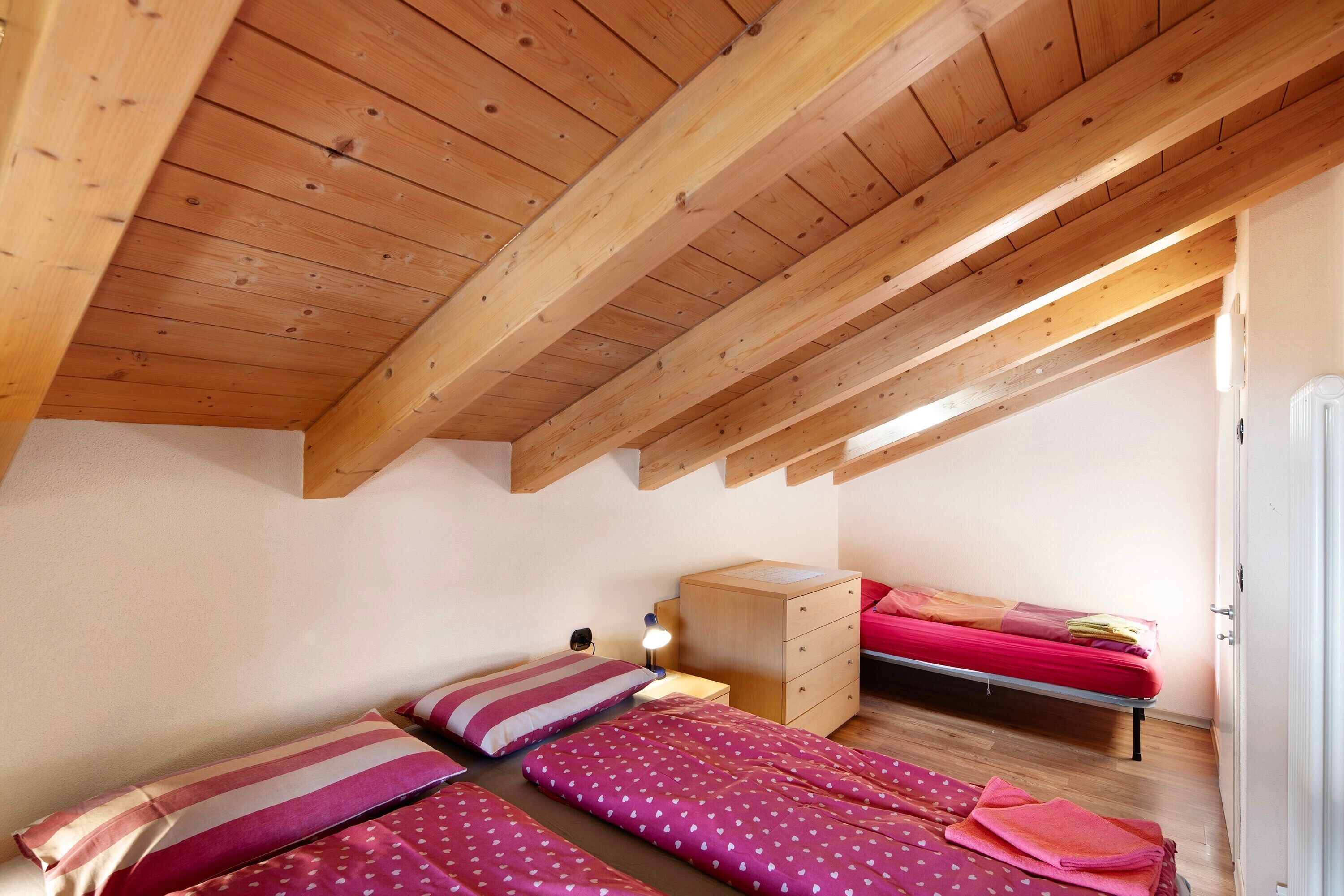 Une chambre avec des poutres en bois, deux lits, une commode et une table de chevet.
