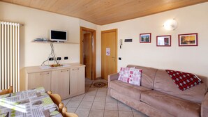 A room with a wooden ceiling, a sofa, a television on a stand, a dining table, and a kitchen area. - Apartment 'Natale 7' with Mountain View, Balcony and Wi-Fi (Livigno)
