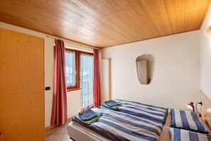 Een slaapkamer met twee bedden, houten plafond, een raam met gordijnen, een spiegel en een bedlampje.