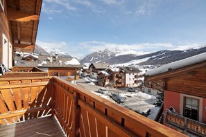 A wooden balcony overlooking a snowy village with buildings and mountains in the background. - Apartment 'Natale 7' with Mountain View, Balcony and Wi-Fi (Livigno)