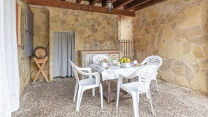 A stone-walled room with a wooden ceiling, a table with chairs, and a small window.