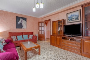 Un salon avec un canapé, un téléviseur, des meubles en bois et un tableau accroché au mur.