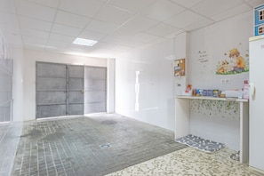 Une pièce avec un sol carrelé, une porte, un mur orné d’une affiche et une étagère sur laquelle sont disposés divers objets.