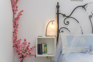 Une chambre à coucher bien rangée, avec une table de chevet, une lampe, une bibliothèque et un lit agrémenté d’un coussin aux motifs bleus et blancs.