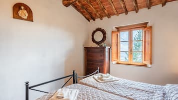 Une chambre avec deux lits, une commode en bois, un miroir et une fenêtre donnant sur des arbres.