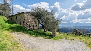 Un edificio de piedra con un sendero de grava, una valla de madera y vistas a montañas distantes.
