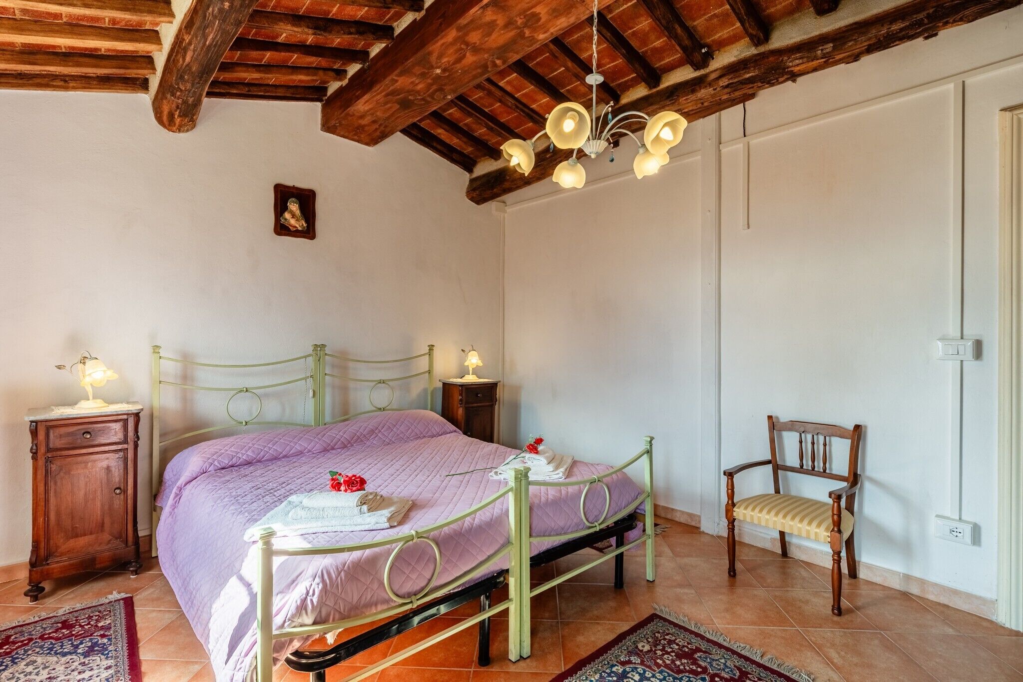 A bedroom with a bed, a wooden chair, a nightstand, a small table, and a ceiling light fixture.