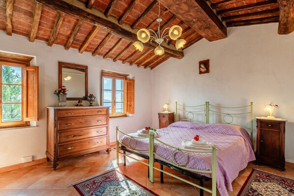 Un dormitorio con techo de madera, una cama con estructura metálica, un aparador, una mesita de noche y un espejo.