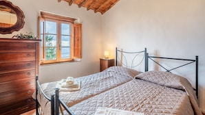 Un dormitorio con techo de madera, una cama con colcha acolchada, un aparador de madera, una mesita de noche con lámpara y una ventana con vistas.