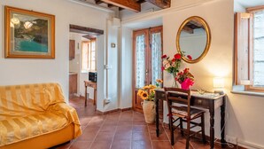 Una habitación con sofá, escritorio con silla, espejo y un jarrón con flores.