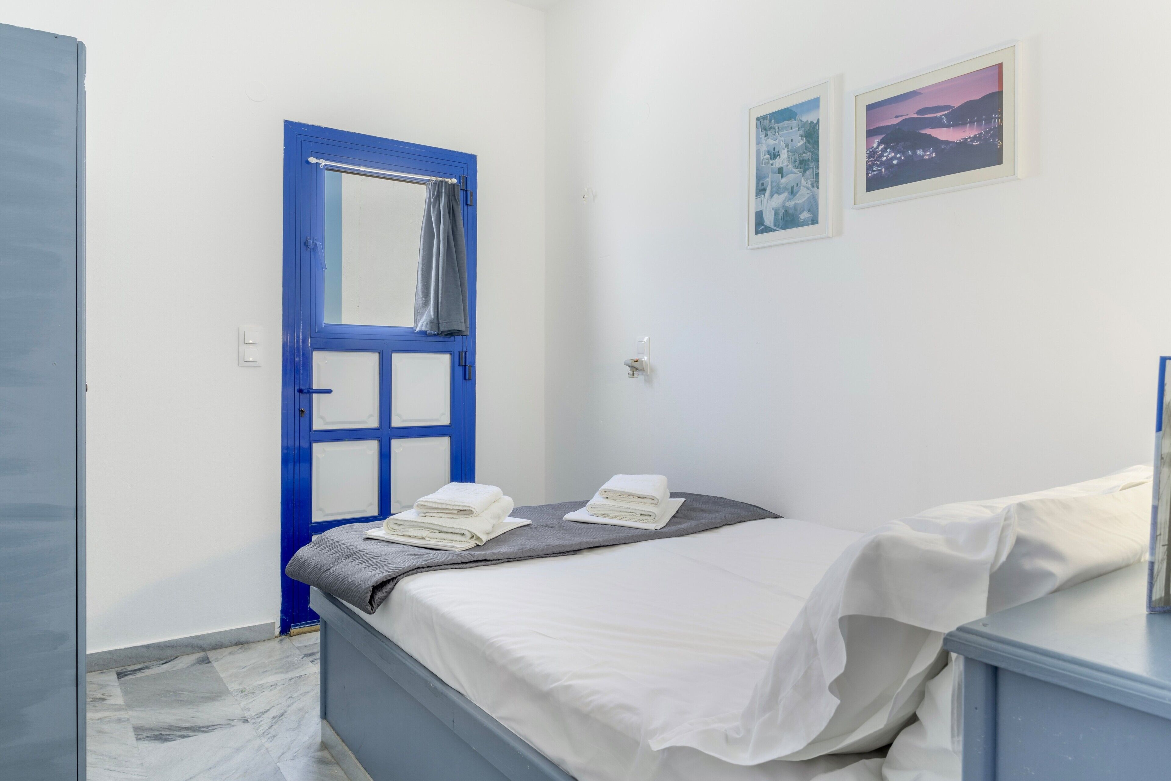 Een slaapkamer met een bed, een blauwe deur, een witte muur en twee prestatiekaders.
