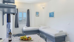 A bedroom with a bed, a table with fruit and a bottle, and a window with curtains. - Apartment '8' with Sea View, Wi-Fi and Air Conditioning (Ios Chora)