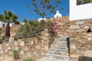 A stone staircase leading to a white building with a bell tower, surrounded by greenery and flowers. - Apartment '2 Studio' with Sea View, Wi-Fi and Air Conditioning (Ios Chora)