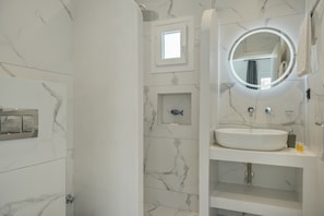 Une salle de bain avec un mur en marbre, un miroir rond, un lavabo et une petite décoration représentant un poisson.