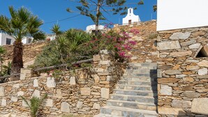 Una escalera de piedra conduce a un edificio blanco con una torre de campanas, rodeado de follaje y flores.