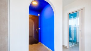 A hallway with a blue wall, a wooden door, and a glass door leading to a balcony. - Bright 1-Bedroom Apartment with Sea View, 10 Minutes from the Beach (Cagnes sur Mer)