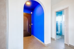 Um corredor com parede azul, porta de madeira e porta de vidro que dá para uma varanda.