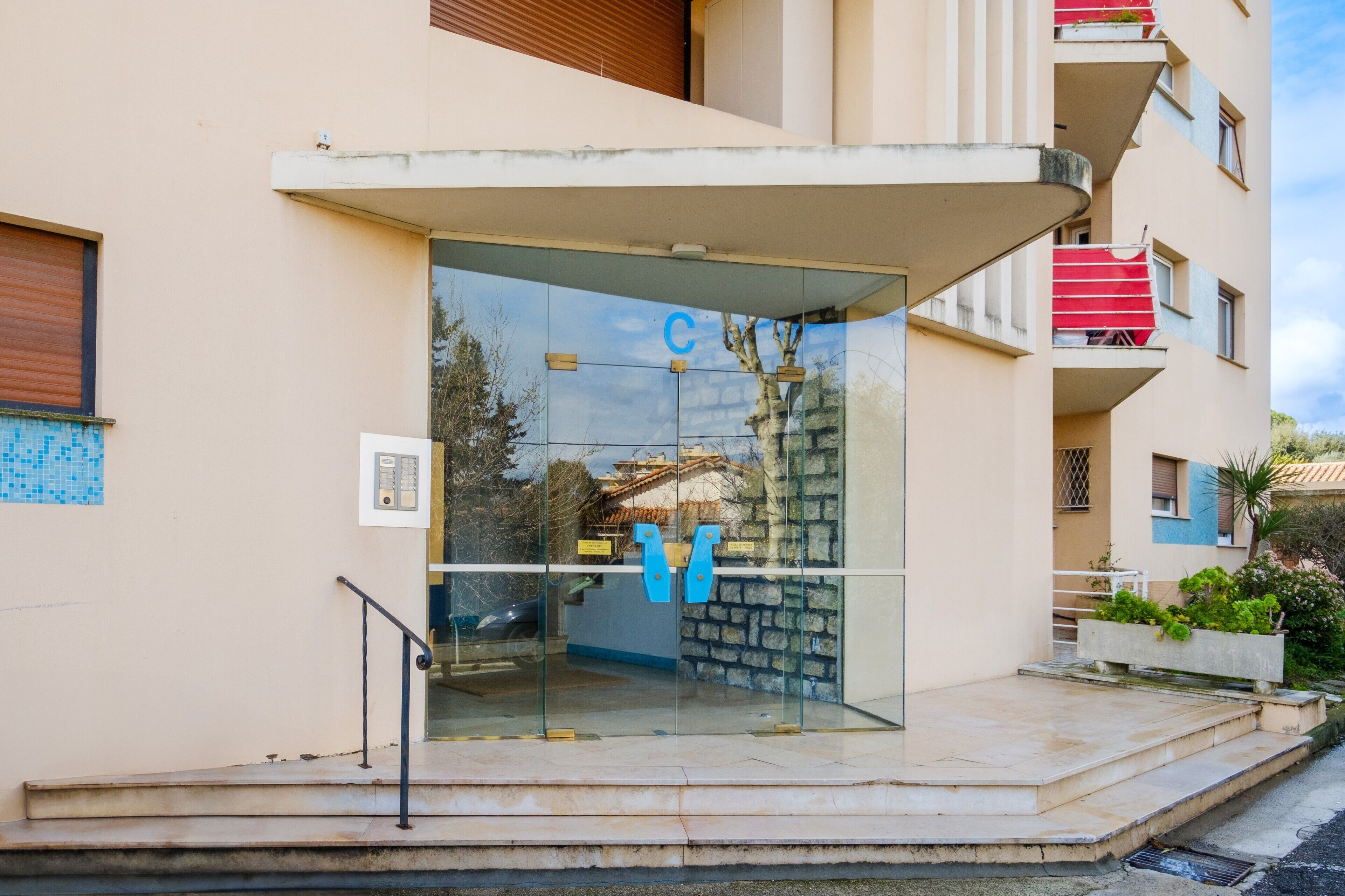 Un edificio moderno con entrada de vidrio, un letrero azul y una pared de piedra.