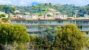 A multi-story building with balconies, a hilly background, and trees in the foreground. - Bright 1-Bedroom Apartment with Sea View, 10 Minutes from the Beach (Cagnes sur Mer)